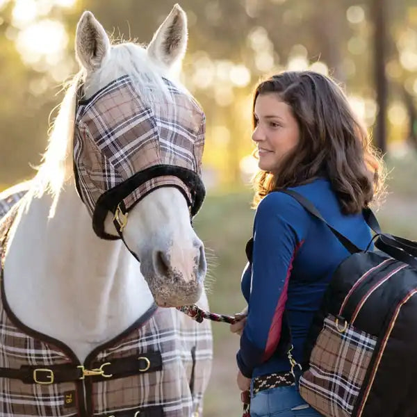 Woman standing with a white horse wearing fly mask and sheet.