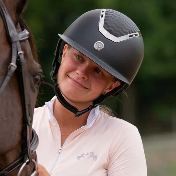 Girl wearing riding helmet looking at horse.